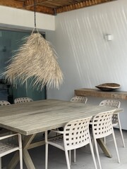 Minimalist exterior featuring natural straw pendant lighting, wooden furniture and neutral tones, inspired by Mediterranean and coastal design. © Laura