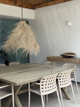 Minimalist exterior featuring natural straw pendant lighting, wooden furniture and neutral tones, inspired by Mediterranean and coastal design.