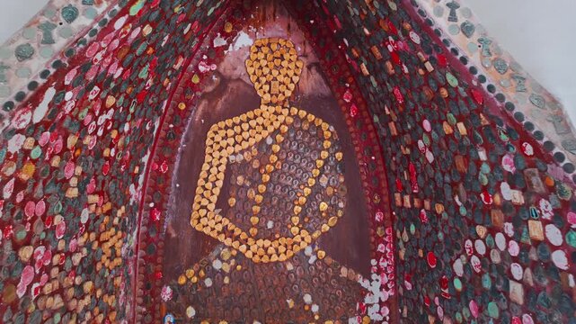 A mosaic of a meditating Buddha made of coins and colorful stones at Wat Sam Phran in Nakhon Pathom, Thailand. This sacred site is a popular pilgrimage destination.