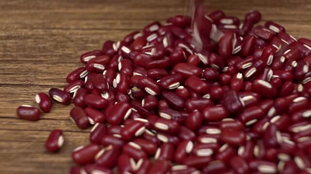 Raw red beans falling and piling onto a textured wooden table surface
