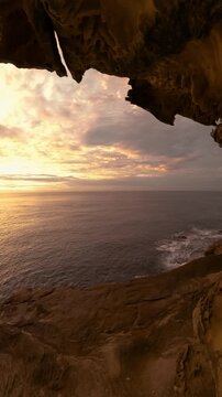 Slow motion fisheye video of sunrise over the ocean framed by a natural rock opening along the Sydney coastline, with calm water reflecting soft golden morning light, Australia.