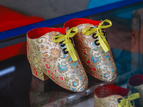 Traditional Chinese lotus shoes for bound feet, featuring elegant floral embroidery, bright yellow laces, and a golden patterned exterior with a contrasting red interior, isolated on a reflective dark