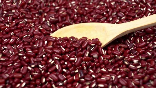 A wooden spoon scooping and pouring red beans to reveal their quality