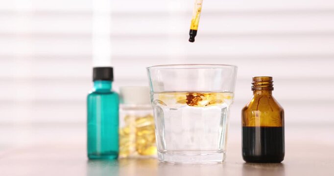 Woman dripping iodine into glass of water from pipette at wooden table, closeup