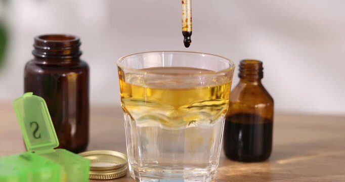 Woman dripping iodine into glass of water from pipette at wooden table, closeup