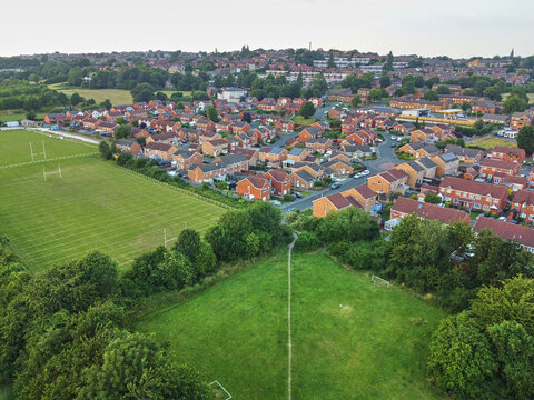 Aerial view of residential housing estate with red brick houses, green playing fields, and lush trees in Dewsbury, West Yorkshire, United Kingdom.