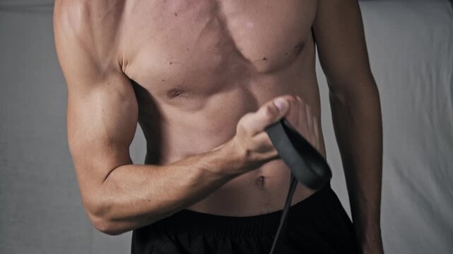 A man with a well-defined physique uses a rubber expander for an arm workout. The footage shows his chest and abdominal muscles flexing during the resistance exercise.