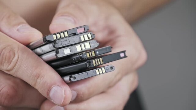 Close-up shot of hands holding a stack of used old lithium-ion batteries from mobile phones. The image depicts e-waste electronic component recycling and disposal.