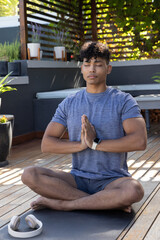 Obraz premium Male meditating with hands in prayer on yoga mat on wooden deck near headphones, smartwatch