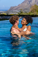 Fototapeta premium Romantic couple holding woman in arms near infinity pool edge, woman wearing striped bikini top