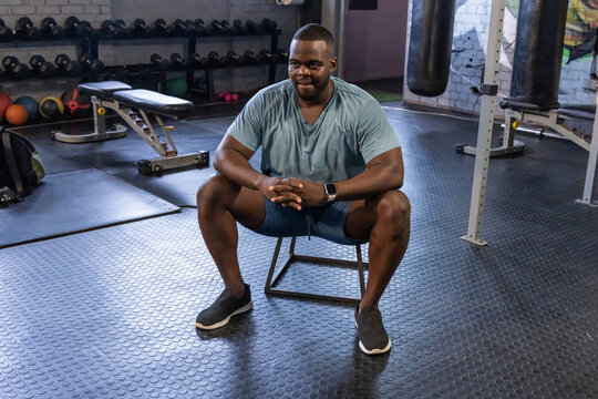 African American man sitting on low plyo box at gym, wearing damp athletic shirt and smartwatch