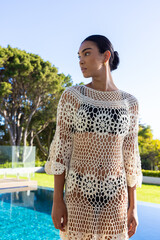 African woman standing poolside wearing cream crochet coverup over black bikini and gold hoops