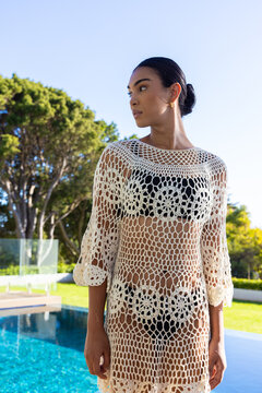 African woman standing poolside wearing cream crochet coverup over black bikini and gold hoops