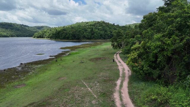 Aerial view of a motorcyclist riding on a dirt road along Huai Khae reservoir bank in Sakon Nakhon, Thailand.