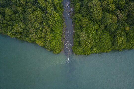 Aerial view of a narrow river merging into a wide main river from above.