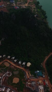 Vertical screen Aerial Construction Site Overview, Scattered Houses At Karst Base, Red Earth Roads And Building Foundations, Emerging Village Expansion Visible From Above