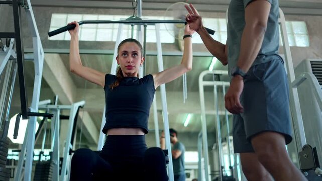 Personal trainer coaching a woman during a lat pulldown exercise on a strength training machine in a professional gym