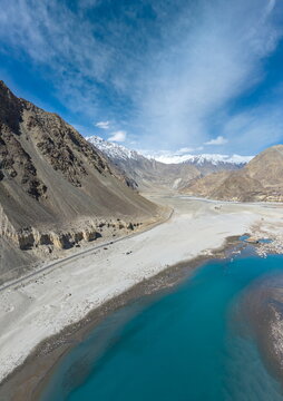 Aerial view of Keris Valley with a turquoise river flowing through sandy banks, flanked by steep, rugged mountain slopes under a clear blue sky in Yugo, Gilgit Baltistan, Pakistan.