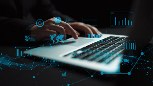 Close-up of hands typing on a laptop, surrounded by digital data visuals and graphs that represent modern technology and business analytics in a creative workspace. Xenic