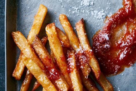 Overhead shot of golden fries arranged on a metal tray with a side of ketchup and sprinkled salt, showcasing a delicious fast food meal presentation