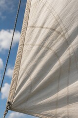 Obraz premium Close-up of sailboat mainsail, heavy canvas billowing taut in wind, visible stitching against soft sky.