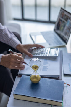 Professional Reviewing Income Tax Report and Expenses in Office with Hourglass on Table. Time Management Concept.