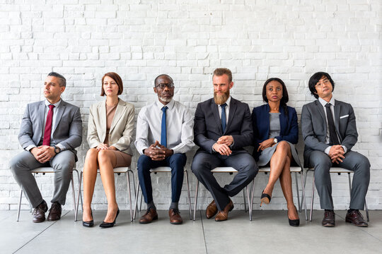 Diverse group of professionals in suits sitting against a white wall.