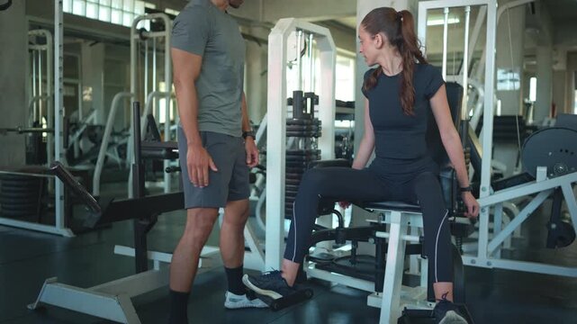 Personal trainer adjusting resistance settings for a client before a strength training session on gym equipment