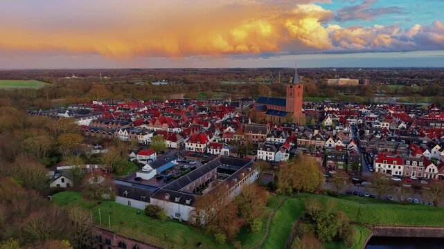 Aerial view of a historic fortified old town with a prominent church tower at sunset. Drone landscape of ancient european architecture and a green star fort moat during golden hour, panorama.