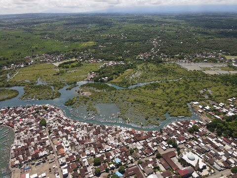 Aerial view of Kuta Lombok, featuring dense residential rooftops, a mosque, and waterways winding through lush mangrove forests, Kuta Lombok, West Nusa Tenggara, Indonesia.