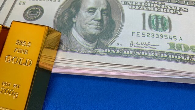 Close-up of a gold bar against stacked 100 dollar bills, purpose for marketing or background