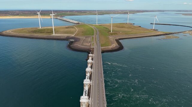 Aerial view of a row of modern offshore wind turbines on a coastal pier. Drone landscape of the Delta Works storm surge barrier and blue sea water in Zeeland, Netherlands, panorama.