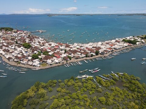 Aerial view of a dense coastal village in Lombok with many small fishing boats moored along the shore and lush mangrove forests in the foreground, Kuta Lombok, West Nusa Tenggara, Indonesia.