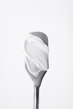 Close up of white cosmetic cream or body lotion smear on metal skincare spatula isolated on white background