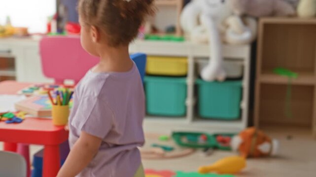 Little hispanic girl reaches up with bare arm to place a yellow marker on a wall activity panel in a daycare building; curiosity discovery.