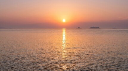 Fototapeta premium The sun sets over a calm ocean, casting a brilliant golden ray across the water. Silhouetted islands appear in the distance, adding depth to the serene scene.