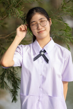 Portrait of a cheerful female student in a traditional Thailand high school uniform, featuring a white short-sleeved shirt with a small bow tie, a navy blue pleated skirt.