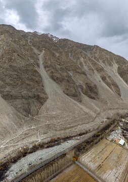 Aerial view of the rugged mountainous landscape near Ghawari, featuring steep rocky slopes, scree, and agricultural fields in the valley in Ghawari, Gilgit Baltistan, Pakistan.