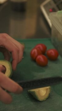 Vertical video. Cooking process. Preparing avocado. Chef hand scooping pulp of green fruit with metal spoon.Man slicing raw fresh ingredient food.
