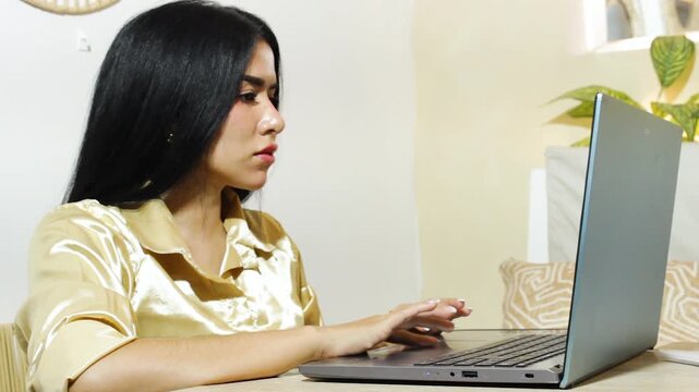 Portrait of a beautiful Latina woman typing on a laptop, dedicated to remote work, content creation, and online learning in a modern office in Neiva, Huila, Colombia. Concept of technology and concent