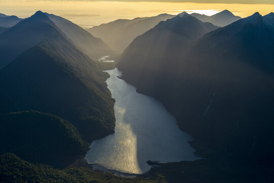 Aerial view of Pumalin Douglas Tompkins National Park featuring a serene lake nestled between lush forested mountains during golden hour in Caleta Gonzalo, Los Lagos, Chile.