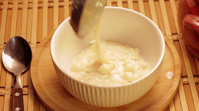 Creamy Brazilian canjica or mungunza being served in a white bowl on a bamboo base. Traditional regional desserts.