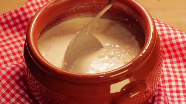 Creamy Brazilian canjica or mungunza being ladled from a brown ceramic pot