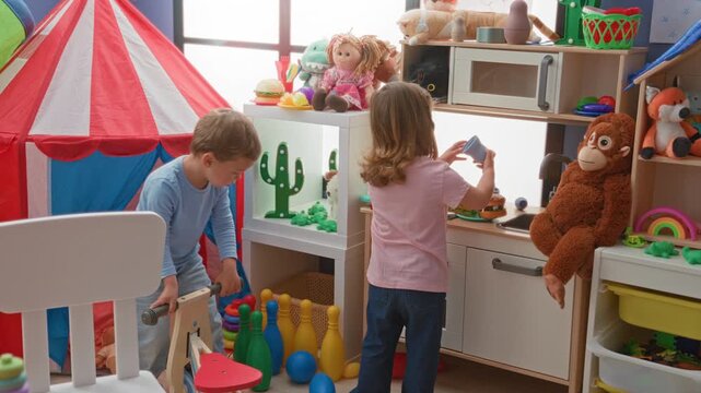 Girl and boy play with toy kitchen, tent, plush monkey while boy bends to pick up bowling pins inside building; playful childhood joy.