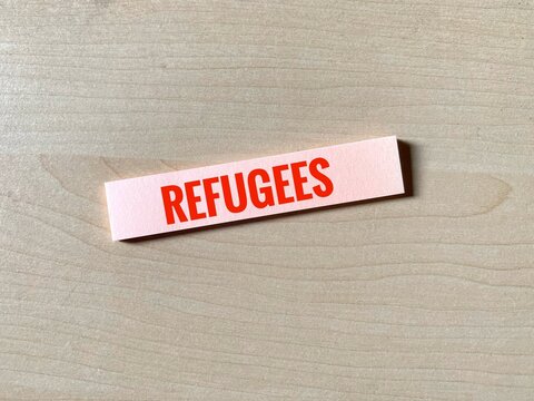 Paper strip with word Refugees against wooden background. Refers to people who have been forced to leave their country in order to escape war, persecution, or natural disaster.