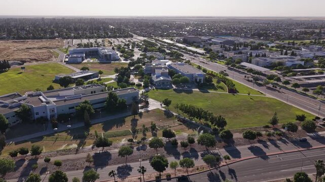Push in drone shot of the Clovis Community College campus, showing its modern buildings, green lawns, parking lots, and the surrounding suburban landscape of Fresno, California