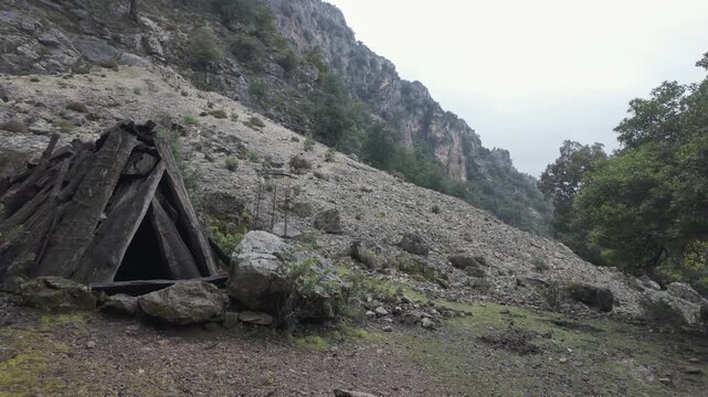 Abandoned stone shelter beneath towering cliffs in Gorropu Canyon Sardinia landscape, historic cultural heritage artifact