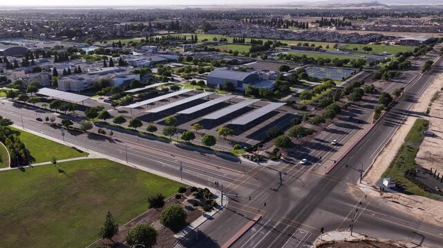 Afternoon sunlight illuminates the sprawling campus of Clovis Community College in Fresno, California, showcasing its modern buildings, large parking lot with solar panels, and athletic fields