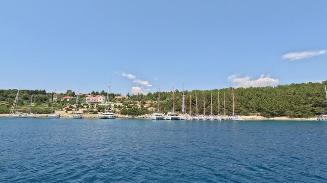 View from a moving boat departing Fiskardo harbor on Kefalonia Island, Greece. Sailing yachts, waterfront villas and pine-covered coastline create a peaceful Mediterranean summer scene in the Ionian