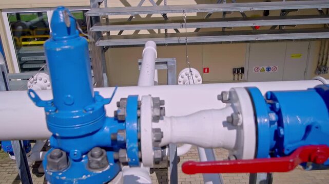Close-up handheld view of an industrial pipeline valve with bolts, flanges and blue metal fittings. Useful for engineering, utility, infrastructure and maintenance themes